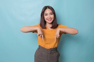 An excited young woman presenting and pointing downwards the copy space, isolated on blue background