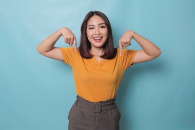 An excited young woman presenting and pointing downwards the copy space, isolated on blue background