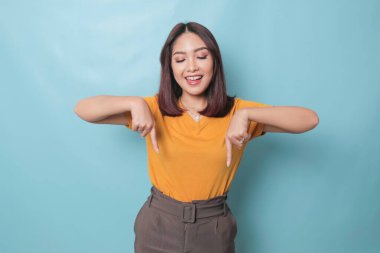 An excited young woman presenting and pointing downwards the copy space, isolated on blue background