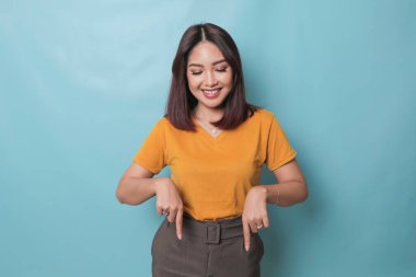 An excited young woman presenting and pointing downwards the copy space, isolated on blue background