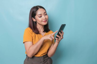 An excited young woman pointing her smartphone in her hand, isolated on blue background