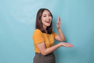 An excited young woman presenting and pointing copy space on her side, isolated on blue background