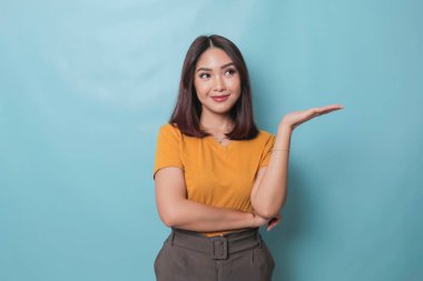 An excited young woman presenting and pointing copy space on her side, isolated on blue background