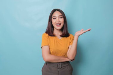 An excited young woman presenting and pointing copy space on her side, isolated on blue background