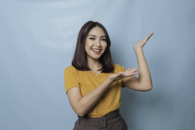An excited young woman presenting and pointing copy space on her side, isolated on blue background