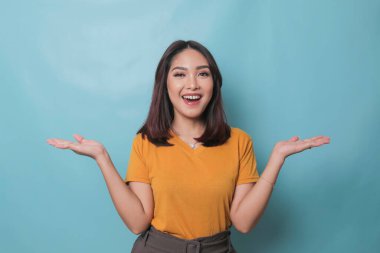 An excited young woman presenting and pointing copy space on her side, isolated on blue background