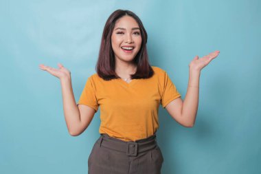 An excited young woman presenting and pointing copy space on her side, isolated on blue background