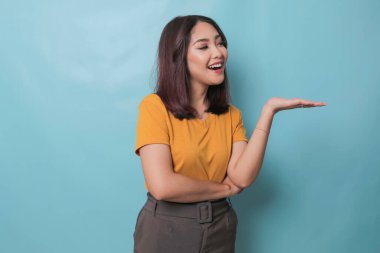 An excited young woman presenting and pointing copy space on her side, isolated on blue background