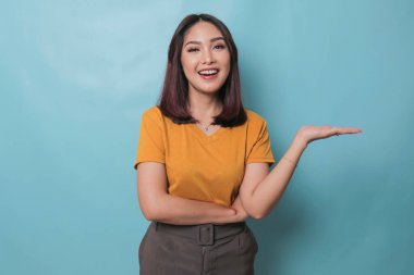 An excited young woman presenting and pointing copy space on her side, isolated on blue background