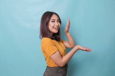 An excited young woman presenting and pointing copy space on her side, isolated on blue background