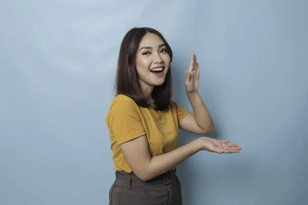 An excited young woman presenting and pointing copy space on her side, isolated on blue background