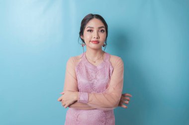 A portrait of Asian woman folding her arms looks upset, wearing modern kebaya isolated by blue background