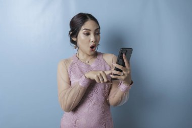 Surprised woman wearing modern kebaya clothes pointing her smartphone