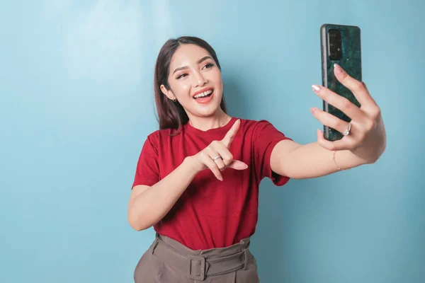 Excited Asian Woman Wearing Red Shirt Pointing Her Smartphone Isolated — Stok fotoğraf