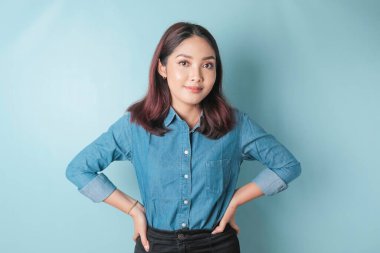 Portrait of a confident smiling girl standing with arms folded and looking at the camera isolated over blue background, wearing a blue shirt