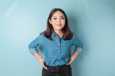 Portrait of a confident smiling girl standing with arms folded and looking at the camera isolated over blue background, wearing a blue shirt