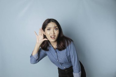 Amazed curious bride young woman wearing a blue shirt trying to hear you overhear listening intently isolated on blue turquoise background studio portrait.