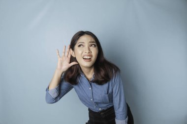 Amazed curious bride young woman wearing a blue shirt trying to hear you overhear listening intently isolated on blue turquoise background studio portrait.