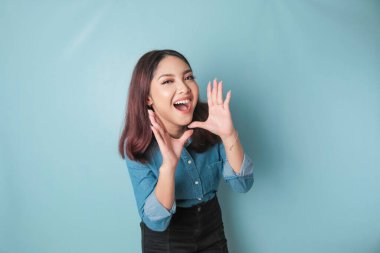 Young beautiful woman wearing a blue shirt shouting and screaming loud to the side with a hand on her mouth. communication concept.