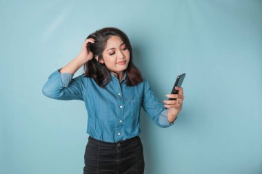 Tired thinking woman, has a sad expression while holding her smartphone. Isolated blue background