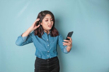 Tired thinking woman, has a sad expression while holding her smartphone. Isolated blue background