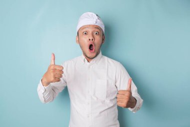 Surprised Balinese man wearing udeng or traditional headband and white shirt, isolated by blue background