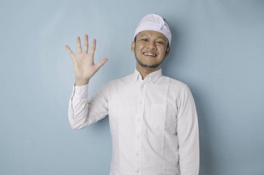 Excited Balinese man wearing udeng or traditional headband and white shirt giving number 12345 by hand gesture