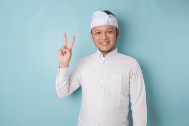 Excited Balinese man wearing udeng or traditional headband and white shirt giving number 12345 by hand gesture