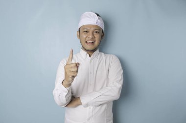 A portrait of a happy Balinese man is smiling wearing udeng or traditional headband and white shirt isolated by a blue background