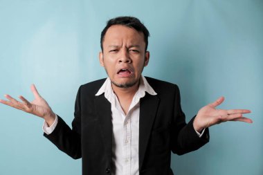 A portrait of Asian businessman wearing black suit look so confuse, isolated by a blue background