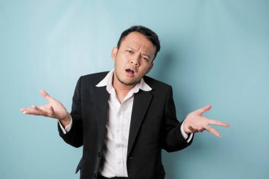 A portrait of Asian businessman wearing black suit look so confuse, isolated by a blue background