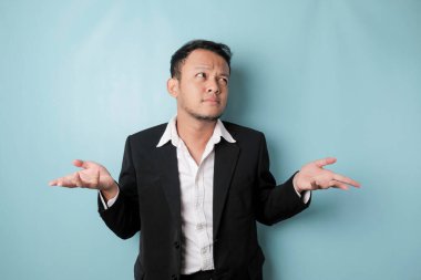 A portrait of Asian businessman wearing black suit look so confuse, isolated by a blue background