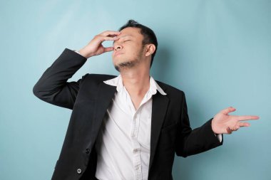 A portrait of Asian businessman wearing black suit look so confuse, isolated by a blue background