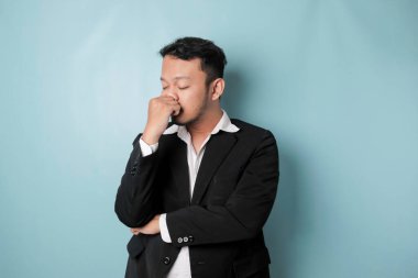 Asian businessman looks tired and depressed, has a sad expression while holding his head. Isolated blue background