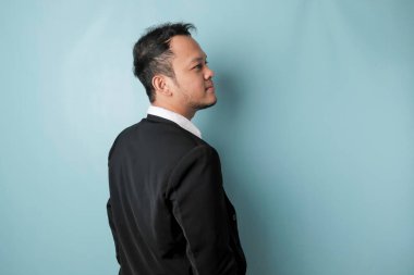 A portrait of a happy attractive Asian man is smiling wearing suit isolated by a blue background