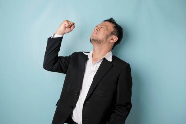 A young Asian man with a happy successful expression wearing suit isolated by blue background