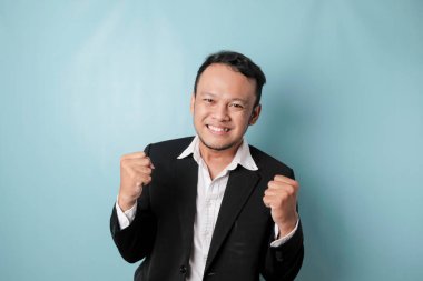 A young Asian man with a happy successful expression wearing suit isolated by blue background
