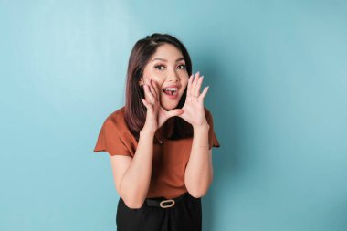 Young beautiful woman wearing a brown shirt shouting and screaming loud to the side with a hand on her mouth. communication concept.