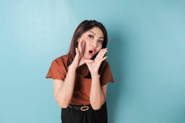 Young beautiful woman wearing a brown shirt shouting and screaming loud to the side with a hand on her mouth. communication concept.
