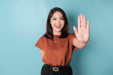 Young Asian woman wearing brown shirt over blue isolated background doing stop sign with palm of the hand.