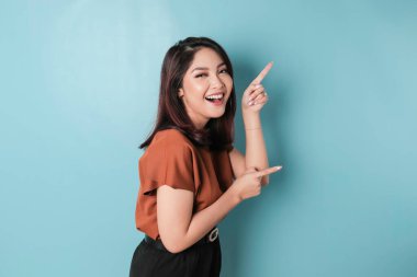 A portrait of a happy Asian woman is smiling and pointing copy space beside her, isolated blue background