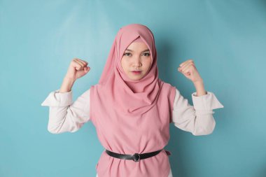 Excited Asian Musllim woman wearing a pink hijab showing strong gesture by lifting her arms and muscles smiling proudly