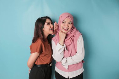 Two young Asian women, hand on mouth telling secret rumor, whispering malicious talk conversation