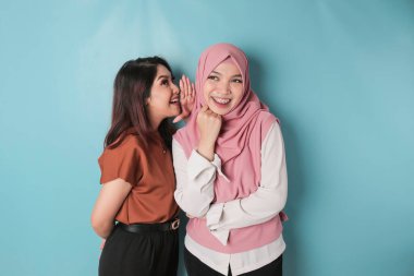 Two young Asian women, hand on mouth telling secret rumor, whispering malicious talk conversation