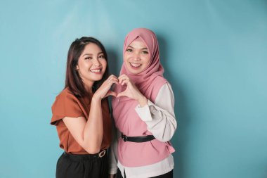 Two attractive young Asian women feels happy and a romantic shapes heart gesture expresses tender feelings and friendship concept