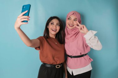 Image of two young happy women friends standing. Looking aside make selfie by phone.
