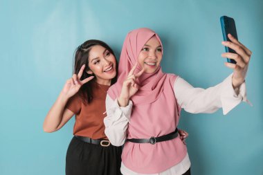 Image of two young happy women friends standing. Looking aside make selfie by phone.