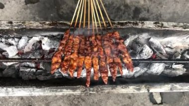 Geleneksel kömür ateşinde tavuk satay. Duman ve iştah açıcı bir bakışla alev alev yanıyordu. Eller ızgarada satay pişiriyor.