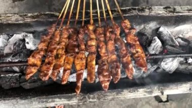 Geleneksel kömür ateşinde tavuk satay. Duman ve iştah açıcı bir bakışla alev alev yanıyordu. Eller ızgarada satay pişiriyor.