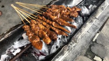 Geleneksel kömür ateşinde tavuk satay. Duman ve iştah açıcı bir bakışla alev alev yanıyordu. Eller ızgarada satay pişiriyor.